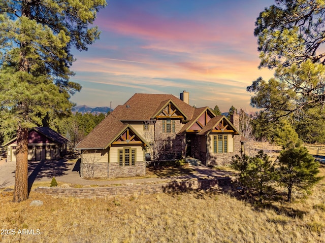 view of front of property featuring stone siding, driveway, a chimney, and a shingled roof