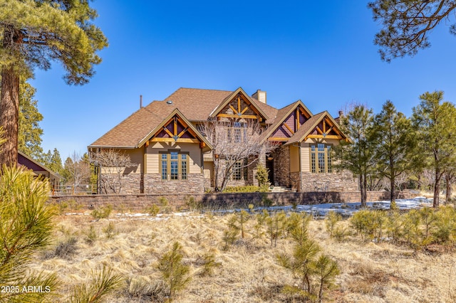 craftsman-style home with stone siding, a chimney, a balcony, and a shingled roof