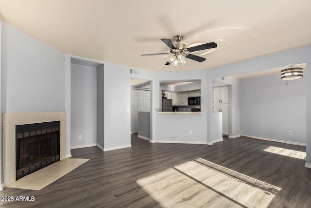 unfurnished living room with a tile fireplace, ceiling fan, and dark wood-type flooring