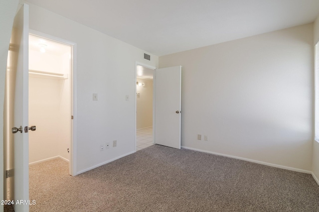 unfurnished bedroom featuring light colored carpet, a closet, and a walk in closet