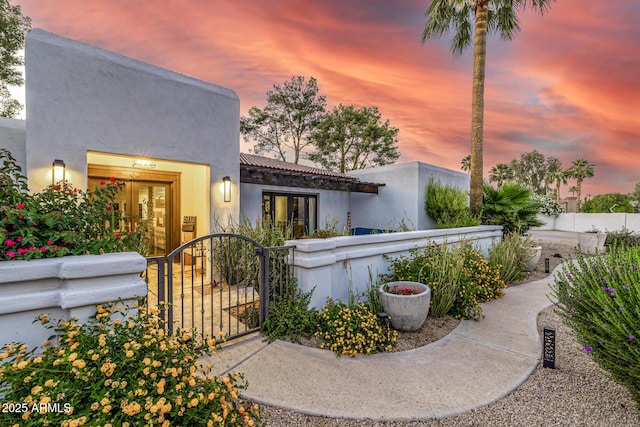 view of front of home featuring fence, a gate, stucco siding, french doors, and a tile roof
