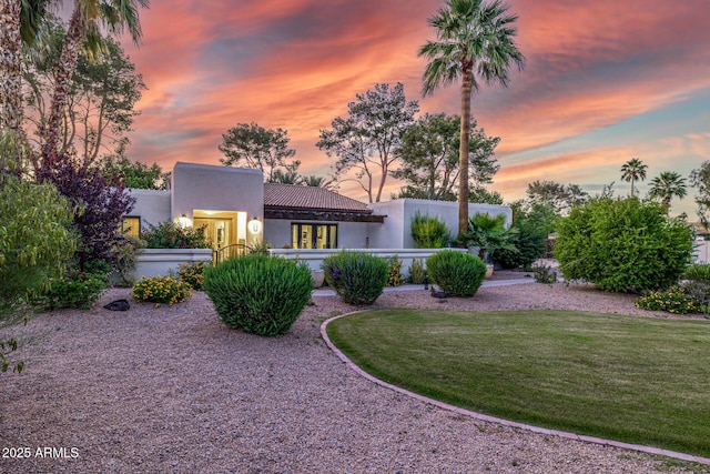 rear view of property featuring stucco siding, a lawn, and a tiled roof