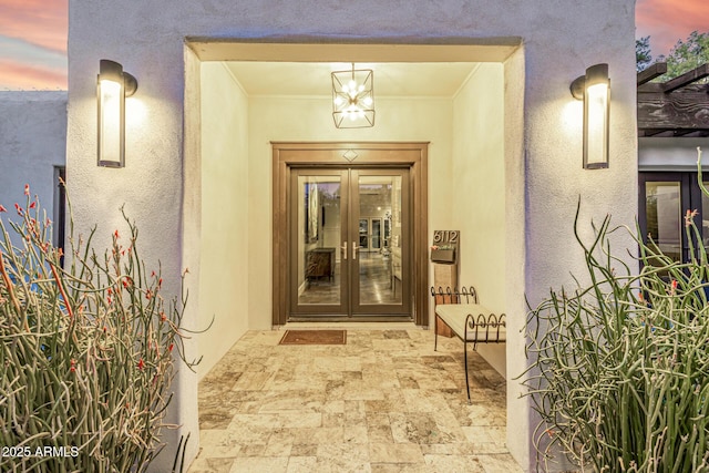 exterior entry at dusk featuring french doors and stucco siding