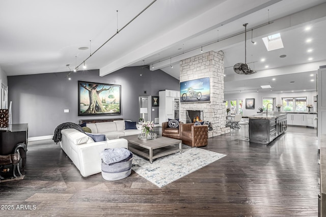 living area with a skylight, dark wood-type flooring, a stone fireplace, track lighting, and baseboards