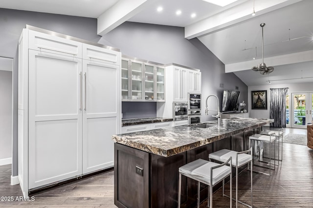 kitchen featuring a sink, dark countertops, a breakfast bar, white cabinets, and an island with sink