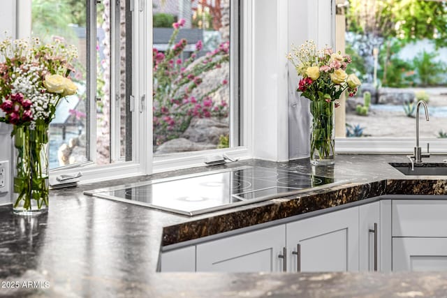 kitchen view of a sink, white cabinetry, black electric stovetop, and dark stone counters