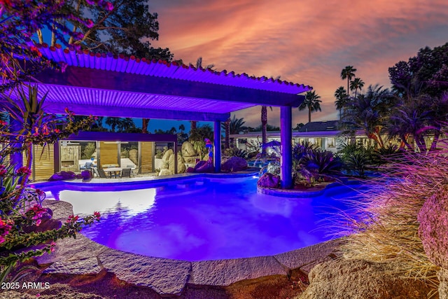 pool at dusk featuring an outdoor pool, an outbuilding, and a patio area