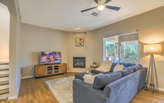 living room with a tiled fireplace, wood-type flooring, and ceiling fan