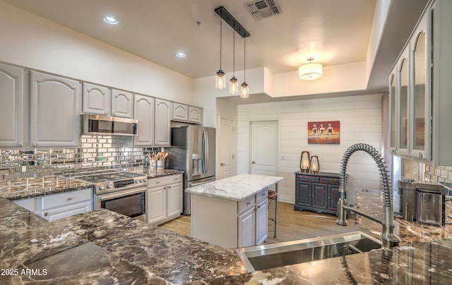 kitchen featuring sink, dark stone countertops, stainless steel appliances, tasteful backsplash, and decorative light fixtures