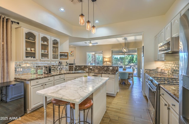 kitchen featuring appliances with stainless steel finishes, white cabinetry, dark stone countertops, a kitchen island, and kitchen peninsula