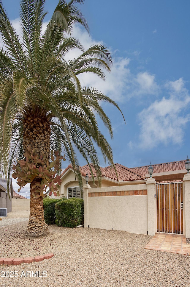 view of side of home featuring stucco siding, a tiled roof, and a gate