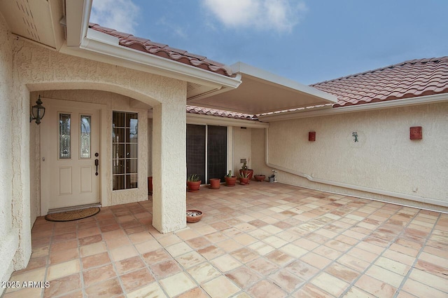 property entrance featuring stucco siding, a patio area, and a tile roof