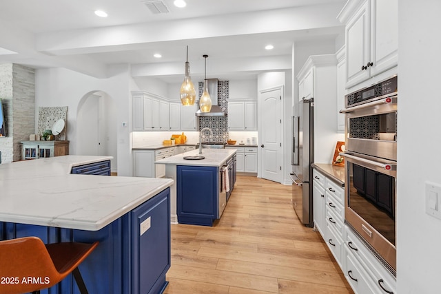 1948 W Paso Trl, Phoenix, AZ 85085 - kitchen featuring blue cabinets, stainless steel appliances, a kitchen island with sink, wall chimney range hood, and white cabinets