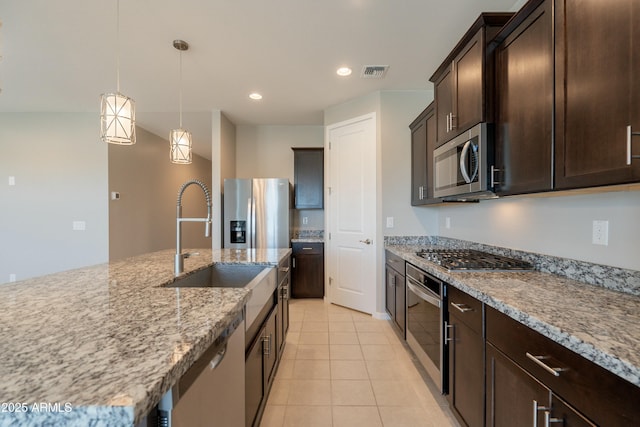 kitchen featuring appliances with stainless steel finishes, visible vents, dark brown cabinets, and light stone counters