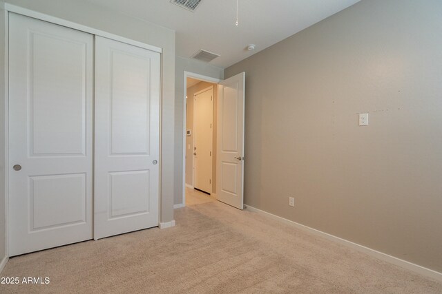 unfurnished bedroom with baseboards, visible vents, light carpet, and a closet