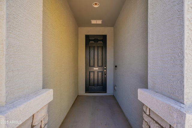 property entrance featuring stucco siding and visible vents