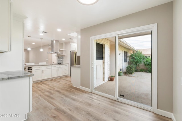 kitchen featuring white cabinetry, light wood-style floors, freestanding refrigerator, island exhaust hood, and pendant lighting