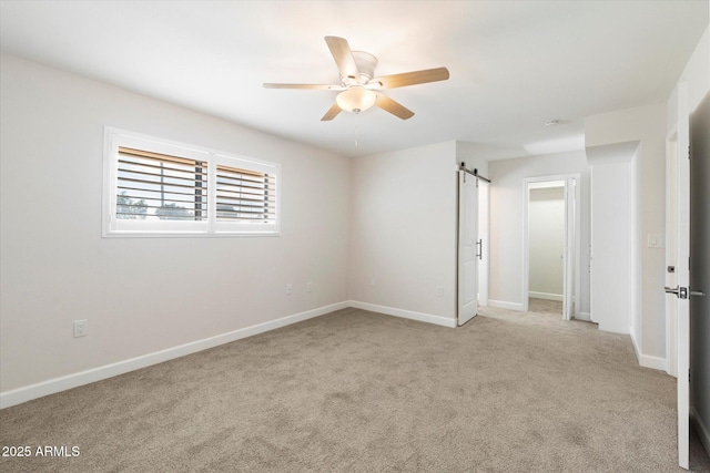 empty room featuring ceiling fan, a barn door, carpet, and baseboards