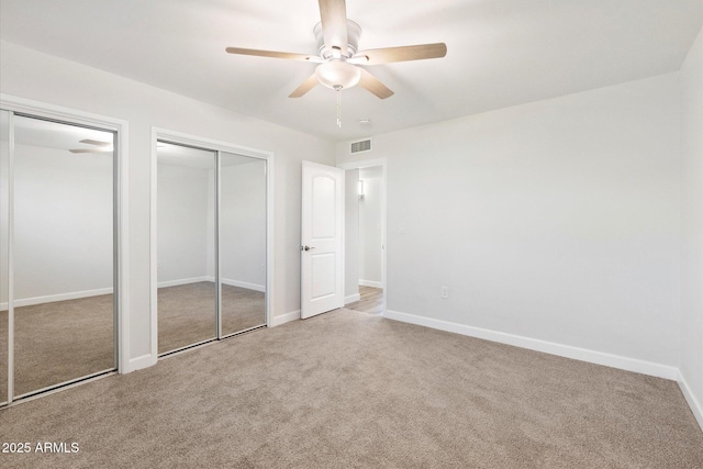 unfurnished bedroom featuring baseboards, visible vents, ceiling fan, carpet, and multiple closets