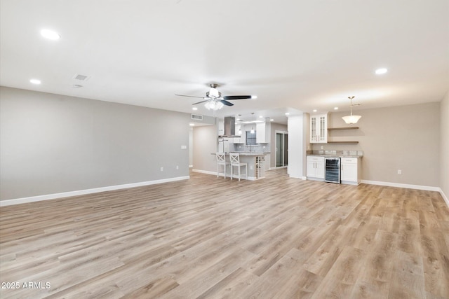 unfurnished living room with light wood-type flooring, wine cooler, baseboards, and recessed lighting