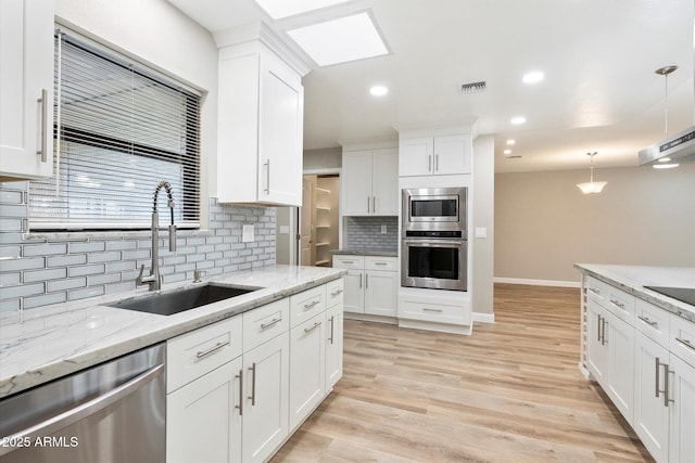 kitchen featuring light wood-type flooring, white cabinets, stainless steel appliances, and a sink