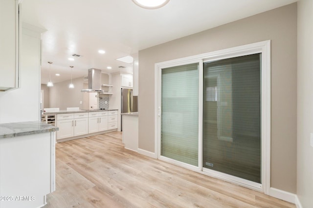 kitchen featuring hanging light fixtures, light wood-style flooring, freestanding refrigerator, white cabinets, and island range hood