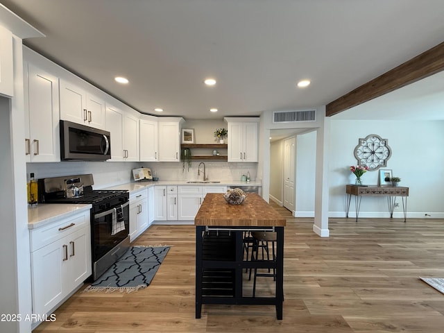 kitchen with visible vents, open shelves, light wood-style flooring, a sink, and appliances with stainless steel finishes