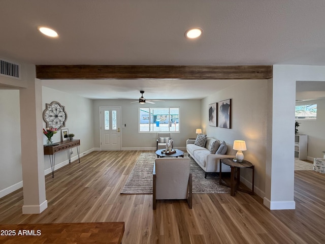 living room featuring beam ceiling, light wood-style floors, visible vents, and baseboards