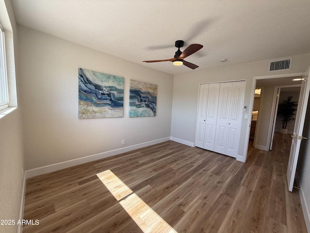 unfurnished bedroom featuring wood finished floors, visible vents, a closet, and baseboards