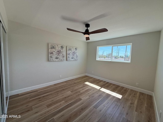 unfurnished bedroom with a closet, baseboards, wood finished floors, and a ceiling fan