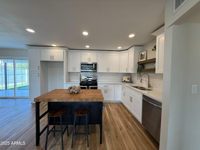 kitchen with a sink, light wood-style flooring, white cabinets, stainless steel appliances, and open shelves