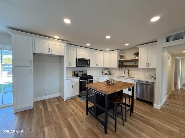 kitchen featuring open shelves, light wood-type flooring, appliances with stainless steel finishes, and white cabinetry