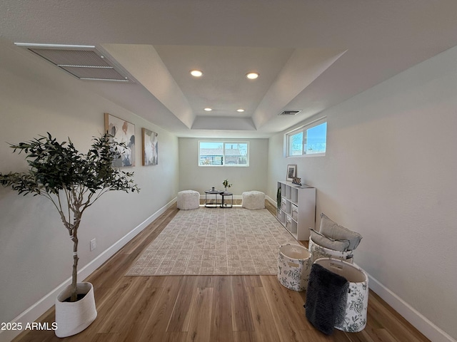 interior space with a raised ceiling, wood finished floors, visible vents, and baseboards