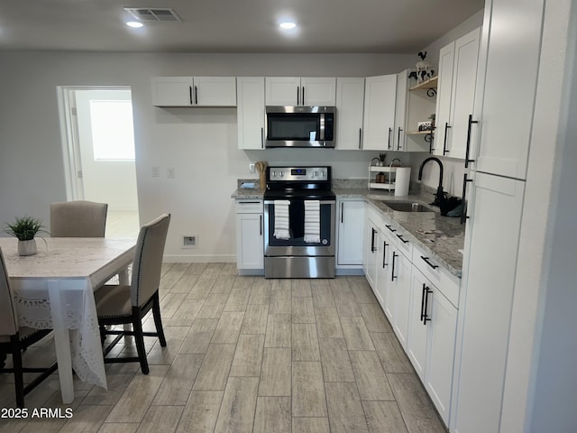 4602 N 47th Ave N, Phoenix, AZ 85031 - kitchen featuring stainless steel appliances, a sink, open shelves, light wood-style flooring, and white cabinets