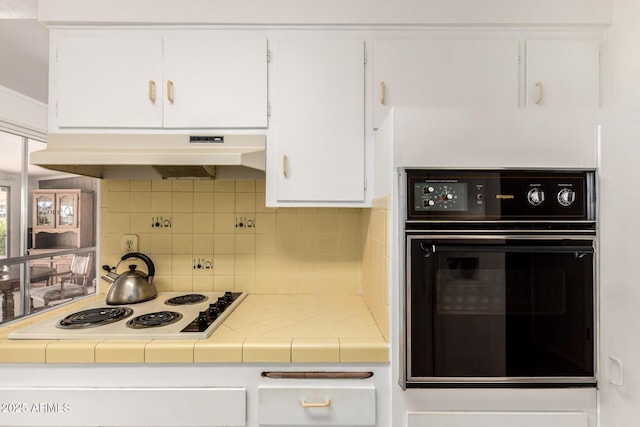 kitchen featuring tile counters, under cabinet range hood, white cabinetry, black oven, and white electric cooktop