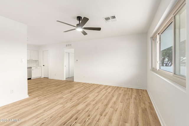 empty room with light wood finished floors, a ceiling fan, visible vents, and baseboards