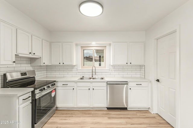 kitchen with stainless steel appliances, light countertops, white cabinetry, a sink, and light wood-type flooring