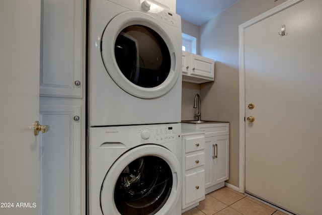 washroom featuring a sink, cabinet space, light tile patterned floors, and stacked washer / drying machine