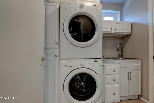 clothes washing area featuring cabinet space, a sink, and stacked washing maching and dryer