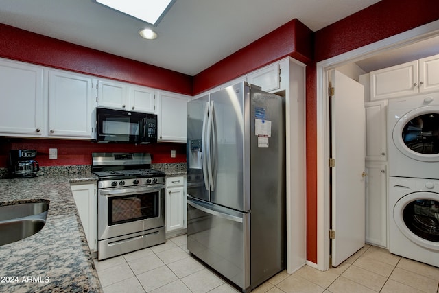 kitchen with stacked washer / drying machine, appliances with stainless steel finishes, white cabinetry, a skylight, and dark stone counters