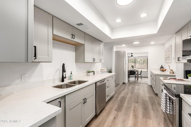 kitchen with light hardwood / wood-style floors, stainless steel appliances, a raised ceiling, sink, and gray cabinets