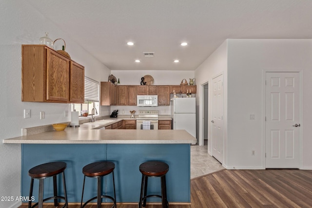 15246 N 138th Ln, Surprise, AZ 85379 - kitchen with brown cabinetry, white appliances, a breakfast bar area, light countertops, and a peninsula