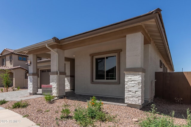 view of front of home featuring stone siding, stucco siding, and fence