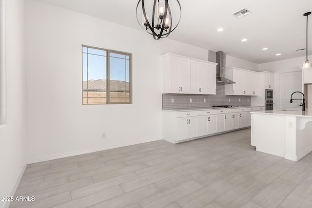 kitchen with a sink, gas stovetop, oven, wall chimney exhaust hood, and visible vents