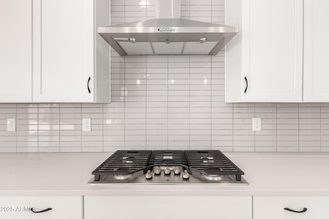 kitchen featuring stainless steel gas stovetop, tasteful backsplash, white cabinetry, wall chimney range hood, and light countertops