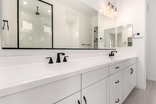 full bathroom featuring double vanity, a tile shower, baseboards, and a sink