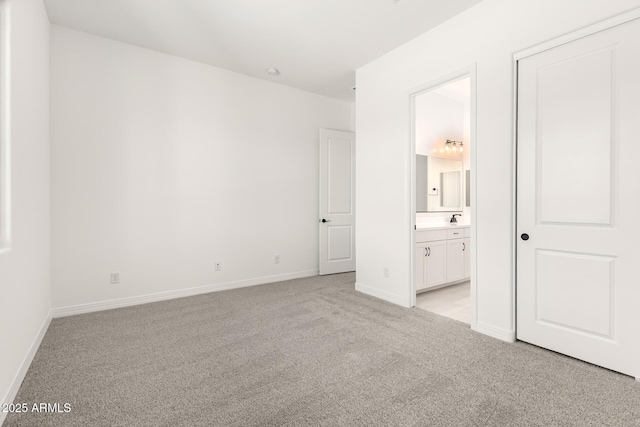 unfurnished bedroom with ensuite bathroom, light carpet, and baseboards