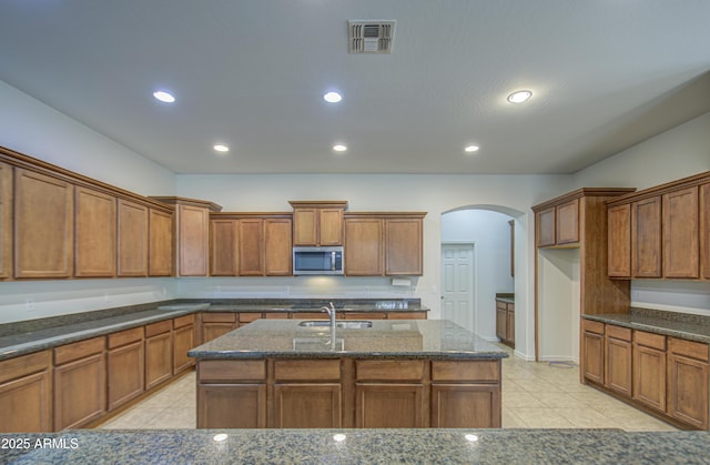 6192 S Claiborne Ave, Gilbert, AZ 85298 - kitchen with dark stone countertops, light tile patterned floors, arched walkways, stainless steel microwave, and brown cabinetry