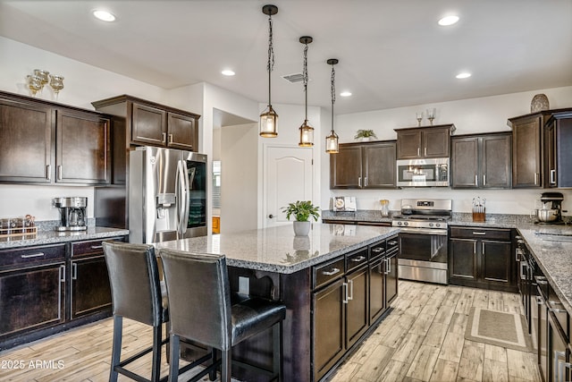 kitchen featuring a kitchen bar, decorative light fixtures, a center island, stainless steel appliances, and light hardwood / wood-style floors