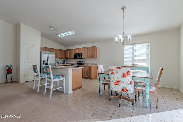 kitchen with light tile patterned flooring, stainless steel refrigerator with ice dispenser, hanging light fixtures, a center island with sink, and range with electric cooktop